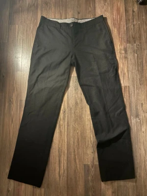 Svarta kostymbyxor med rak passform - Snygga svarta kostymbyxor med klassisk rak passform och diskreta sidfickor. Byxorna har bälteshällor och stängs med knapp och dragkedja. Perfekt för bröllop och andra festligare tillfällen!