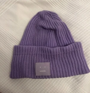 Acne mössa - Lila acne mössa. Enda defekterna: två små hål. Ett innanför mössan som ej syns och ett på uppvikningen som knappt syns. Liten sminkrand på mössan (går säkert bort). 56cm. Köpte second hand för ett tag sen så kan ej garantera äkthet 100% men den ser äkta ut.