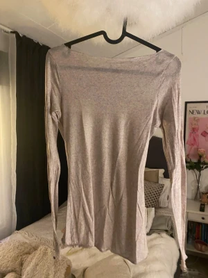 Ljusgrå långärmad topp - En enkel och stilren ljusbeige långärmad topp med offshoulder-skärning. Toppen är figurnära och tillverkad i ett mjukt bomullsmaterial som känns skönt mot huden. Perfekt att matcha med jeans eller kjol för en clean look.