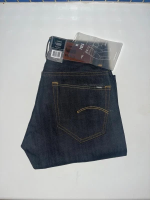 G-Star RAW jeans - Snygga mörkblå jeans från G-Star RAW, modell 3301 Tapered. Jeansen har en smalare passform med avsmalnande ben och är tillverkade i slitstarkt denimtyg. Midja 34cm, längd 100cm. JAG SKICKAR EJ FLER BILDER NÄR JAG BÄR JEANSEN! för storleksguide hänvisar jag till måtten och för bättre inblick i passformen rekommenderar jag att googla på modellnamnet. kolla måtten noggrant :) 74