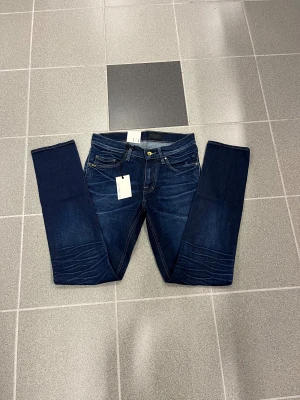 Mörkblå slimmade jeans från tiger of swedenW28 L32 - Snygga mörkblå jeans från Tiger of sweden med raka ben och smal fot. Klassisk femficksmodell med kontrastsömmar och läderpatch bak i midjan. Jeansen har en stilren look och är tillverkade i slitstarkt denimtyg. Modellen heter pistolero 