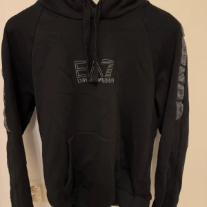 Armani Hoodie - En Armani hoodie i svart färg och med gråa detaljer på bröstet samt armarna. Storlek S