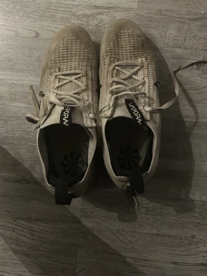Nike Vapormax vita sneakers - Säljer ett par Nike Vapormax sneakers i vitt med stickad ovandel och klassisk svart Swoosh på sidan. Skorna har snörning och genomskinlig sula med synliga luftbubblor för extra komfort. Perfekta för dig som gillar sportig och modern stil. Har en fläck på höger foten, 