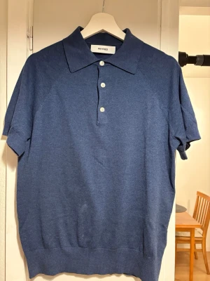 Blå pikétröja från Whyred, storlek S - Snygg blå pikétröja från Whyred i storlek S. Tröjan har klassisk krage, tre knappar framtill och korta ärmar. Materialet är en skön mix av bomull, linne och polyester som ger en mjuk och luftig känsla. Perfekt för dig som gillar stilrena och enkla plagg.