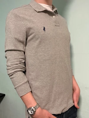 Ralph Lauren långärmad Piké - Säljer en snygg grå  Ralph Lauren långärmad piké. Den är i mycket bra skick. Modellen är M custom slim fit. Har du några frågor? Tveka inte att höra av dig. Allt gott från Deluxe garderoben ⭐️