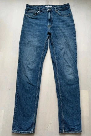 Blå jeansbyxor från Cubus, regular fit - Säljer ett par klassiska blå jeansbyxor från C i regular fit. Modellen har raka ben, fem fickor och en snygg brun patch med '1979' bak på midjan. Jeansen är tillverkade i slitstarkt denim och har en tidlös look med normal passform.