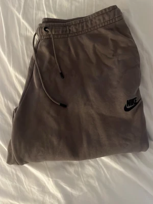 Bruna mjukisbyxor  - Säljer ett par bruna mjukisbyxor från Nike med svart logga på benet. Byxorna har dragsko i midjan för skön passform och är gjorda i mjukt bomullsmaterial. Perfekta för chill dagar eller till och från gymmet!