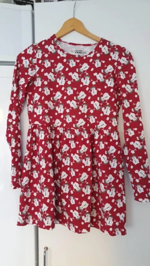 Klänning - Supergullig röd klänning från Mywear Young med snögubbar över hela tyget. Klänningen har lång ärm, rund hals och en utställd kjol. Perfekt för julens alla tillfällen och ger riktiga vintervibes!