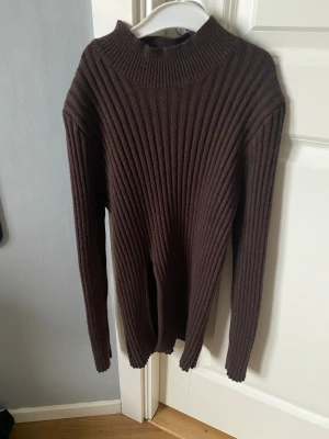 Brun ribbad polotröja med lång ärm - Säljer en brun polotröja med ribbad struktur och lång ärm. Tröjan har en högre hals och är gjord i ett mjukt stickat material som känns skönt mot huden. Perfekt för dig som gillar en clean och chill look med lite edge.