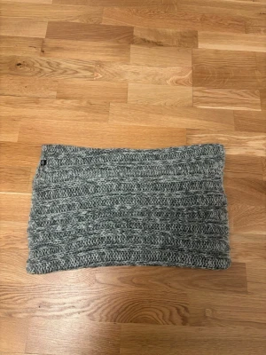 Grå stickad halsvärmare från lager  - Säljer en ribbstickad grå halsvärmare från lager 157. Den är gjord i mjukt garn och har ett snyggt, grovt stickat mönster som ger en chill vibe. Perfekt att dra över huvudet när det är kallt ute. Passar dig som gillar enkel och stilren accessoar.