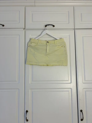 Ljusgul jeanskjol med rå kant - Snygg ljusgul kort jeanskjol med femficksmodell och rå, fransig kant nedtill. Kjolen har knapp och dragkedja framtill samt bälteshällor. Perfekt för dig som gillar en enkel men trendig look.