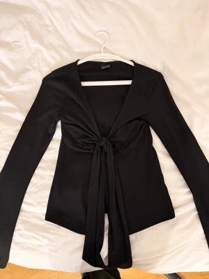 Svart långärmad topp med knyt - Säljer en svart långärmad topp från Gina tricot med snygg v-ringning och knyt framtill. Knappt använd 