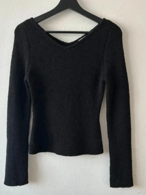 Svart stickad tröja med v-ringning H&M - Svart stickad tröja från H&M i storlek S. Tröjan har en snygg v-ringad hals och långa ärmar. Materialet är mjukt och lite fluffigt, perfekt för att hålla värmen. Passformen är normal och modellen är enkel men stilren.