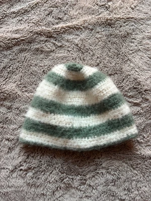 Randig stickad mössa i ullmix - Mysig stickad mössa med breda ränder i vitt och ljusgrönt. Den är fluffig och virkad på alpacka garn. 29cm rakt över