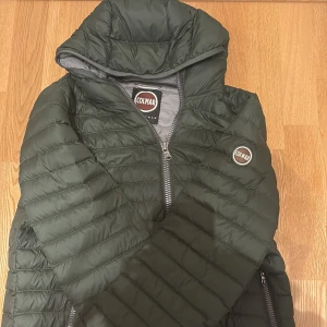 Mörkgrön pufferjacka från Colmar - Säljer en mörkgrön pufferjacka från Colmar med huva och snygga quiltade sömmar. Jackan har dragkedja framtill och två sidofickor med dragkedja. Klassisk Colmar-logga på ärmen och insidan. Perfekt för kyliga dagar!