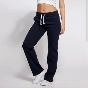 Mörkblå mjukisbyxor med snörning - Mörkblå mjukisbyxor med vit snörning i midjan och raka ben. Byxorna har en avslappnad passform och är tillverkade i mjukt bomullsmaterial, perfekta för chill dagar. Snygg och enkel design som funkar till sneakers.