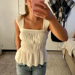 Vit blus med volang - Supersöt vit blus med breda axelband, smockad överdel och volang nertill.  Perfekt till jeans eller kjol🤗använd några gånger men inga synliga defekter!