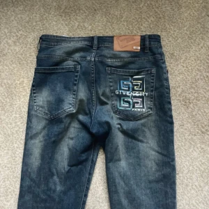 Blå jeans från Givenchy med broderi - Säljer ett par blå jeans från Givenchy med snyggt broderat logomönster i flera färger på bakfickan. Jeansen har klassisk femficksdesign, knapp och dragkedja framtill samt en cool tvättad look. Perfekta för dig som vill sticka ut med designerjeans.