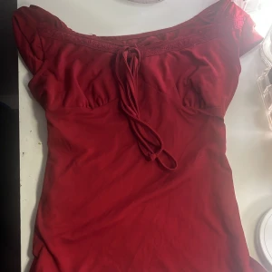 Röd kort klänning med spets och snörning - Supersöt röd kort klänning med spetsdetaljer längs urringningen och snörning framtill. Klänningen har en figurnära passform och är tillverkad i ett mjukt material som känns skönt mot huden. Perfekt för dig som vill sticka ut med en feminin och trendig look.