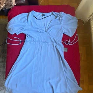 Ljusblå omlottklänning Vero Moda M - Supersöt ljusblå omlottklänning från Vero Moda i storlek M. Klänningen har puffiga korta ärmar, v-ringning och knytband i midjan. Tillverkad i ett mjukt, lätt material och stängs med dragkedja i sidan. Perfekt för dig som gillar en feminin och fräsch stil. Bara en användning men armband har fastnat lite på den men syns knappt, sedan har sömmen där man sätter fast knytbandet gått lite sönder men de jätte enkelt att sy nytt.