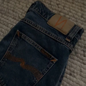 Marinblå Nudie Jeans 30/32 (Oanvända)  - Säljer ett par mörkblå jeans från Nudie Jeans i klassisk rak modell. Jeansen har snygga kontrastsömmar och Nudie-loggan på bakfickan. Tillverkade i slitstarkt bomullstyg och passar perfekt till en avslappnad stil.