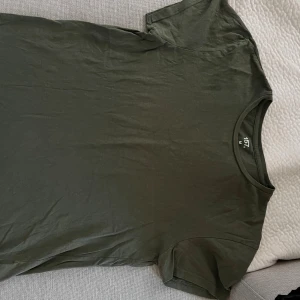 Mörkgrön t-shirt från 157 i bomull - En basic mörkgrön t-shirt från 157 i 100% bomull. Klassisk rund halsringning och korta ärmar, perfekt för en clean och avslappnad stil. Passar dig som gillar enkla plagg med snygg passform.