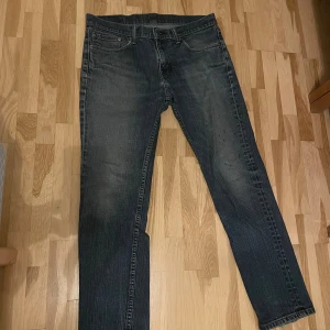 Levi's 511 mörkblå jeans straight fit - Mörkblå Levi's 511 jeans med klassisk femficksdesign och diskret slitning på låren. Jeansen har raka ben och normal passform, tillverkade i robust denim med snygga kontrastsömmar och den ikoniska röda Levi's-taggen på bakfickan. 