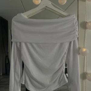 Vit offshoulder långärmad topp - Säljer en stilren vit offshoulder topp med långa ärmar. Toppen har en bred, vikt kant över axlarna som ger en snygg och trendig look. Perfekt att matcha med jeans eller kjol för en clean och fräsch outfit. Aldrig använd.