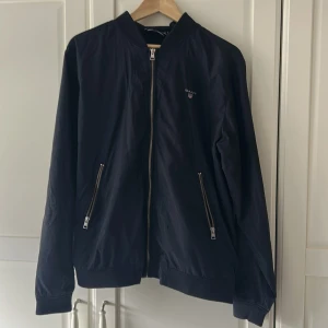 Marinblå jacka från GANT - Snygg marinblå bomberjacka från GANT i storlek L. Använd få antal gånger