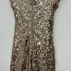 Glittrig guldig paljettklänning - Supersnygg kort klänning täckt av guldiga paljetter som verkligen glittrar. Modellen är figurnära med korta ärmar och dragkedja i ryggen. Perfekt för dig som vill sticka ut och glänsa. Materialet är syntet och klänningen har en lyxig känsla.