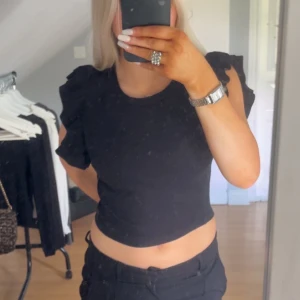 Svart croppad topp med volangärm Zara - Svart croppad topp från Zara med volangdetaljer på axlarna. Toppen är ribbad och har en rund halsringning. Materialet är mjukt och stretchigt för en bekväm passform. Den är inte super mycket använd men rätt mycket dock ser man inget på den