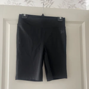 Svarta cykelshorts  - Svarta cykelshorts med hög midja och tight passform. Perfekta för träning eller en sportig look. Tillverkade i stretchigt syntetmaterial som andas och ger bra rörelsefrihet.