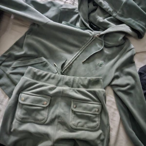 Grönt velour set från Juicy Couture xs-s - Mjuk och lyxig ljusgrön hoodie från Juicy Couture i velour med dragkedja, huva och snörning. Ikonisk JC-logga broderad på bröstet och snygga detaljer i silver. Perfekt för en chill och trendig look. Storlek s. Byxorna i storlek xs, allt i jättefint skick!