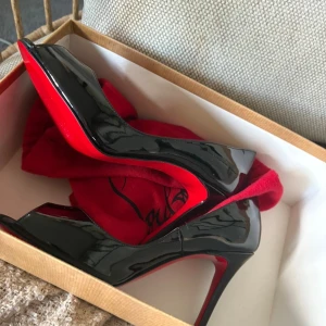 Christian Louboutin svarta lackpumps - Säljer ett par ikoniska svarta pumps från Christian Louboutin i lackat skinn med klassisk röd sula. Skorna har öppen tå och hög klack, perfekt för dig som vill sticka ut. Kommer med originalpåse. Riktigt lyxiga och snygga detaljer.
