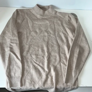 Beige tröja med rutmönster - Snygg beige tröja med diskret rutmönster och ribbade muddar. Tröjan har lång ärm och är stickad i mjukt material, perfekt för kyligare dagar. Enkel att matcha med jeans. Passar runt 10-12 åringar, hör av dig vid frågor 