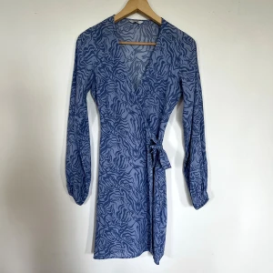 Blå omlottklänning med zebramönster - Omlottklänning med v-ringning och knyt i midjan. En aning liten för mig som brukar ha S-M i klänningar