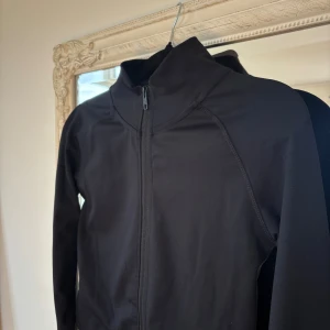 Svart sportig jacka - Svart, stilren träningsjacka med hög krage och hel dragkedja framtill. 