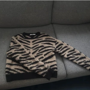 Beige och svart zebramönstrad tröja - Säljer en snygg stickad tröja från H&M med zebramönster i beige och svart. Tröjan har rund halsringning, långa ärmar och ribbade muddar vid ärmslut och nederkant. Perfekt för dig som vill sticka ut med en trendig look.