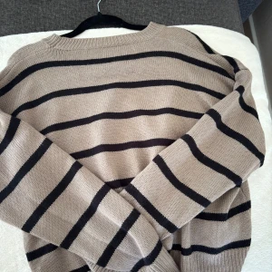 Beige och svart randig stickad tröja - Snygg stickad tröja i beige med svarta horisontella ränder. Tröjan har rund halsringning och långa ärmar. Perfekt för lager-på-lager och chill dagar. Enkel att matcha med jeans  eller kjol.