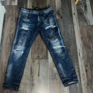 Blå distressed jeans Supply & Demand - Snygga blå jeans från Supply & Demand med slitna detaljer och coola revor framtill. Jeansen har en smal passform och klassisk femficksdesign. Färgskiftningar och slitningar ger ett trendigt, street-inspirerat uttryck. Perfekta för dig som gillar en edgy stil.