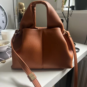 Brun handväska från Polène i skinn - Säljer en snygg brun handväska från Polène i mjukt, strukturerat skinn. Väskan är i färgen Camel i storlek mini. Aldrig använd. Säljer då färgen inte passade mig☺️dustbag följs med