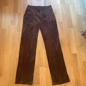 Bruna velourbyxor Juicy Couture S - Mysiga bruna velourbyxor från Juicy Couture med bred resår och snörning i midjan. Byxorna har raka ben, stora fickor fram och bakfickor med knappdetalj. Storlek S och i väldigt bra skick💕