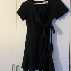 Svart omlottklänning  - Svart kort omlottklänning med knyt i midjan i stl 36 men skulle mer säga att den är xs.
