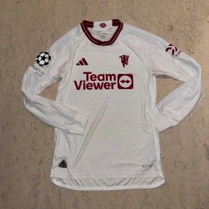Manchester United vit långärmad tröja - Manchester Uniteds officiella bortatröja 23/24 från Adidas. Vit med vinröda detaljer, långärmad och tillverkad i lätt funktionsmaterial. Broderad klubbmärke, Champions League-märke på ärmen och TeamViewer-logga på bröstet. Slimmad passform och autentisk badge. Nypris 1200kr mitt pris 499kr