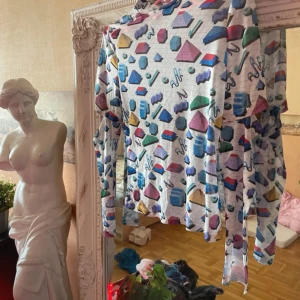 Top No°1 - Säljer en långärmad topp med vit bas och färgglatt geometriskt mönster i blått, lila, rött, grönt och gult. Tunt och stretchigt material, perfekt för dig som gillar unika prints och vill sticka ut. Hög hals och figurnära passform.