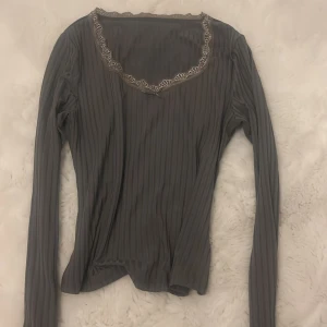 Grå ribbad långärmad topp med spets - Säljer en grå långärmad topp med ribbad struktur och v-ringning. Toppen har fina spetsdetaljer längs halsringningen och vid ärmsluten, vilket ger en söt och trendig look. Perfekt att styla med jeans eller kjol för en chill vibe.