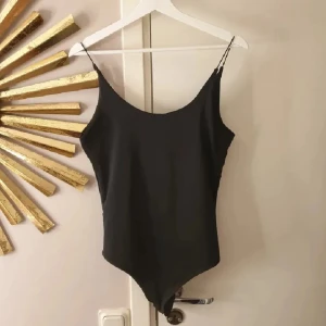 Svart body med smala axelband - Snygg svart body med smala axelband och enkel, stilren design. Modellen har en klassisk form med rundad halsringning och hög benskärning. 
