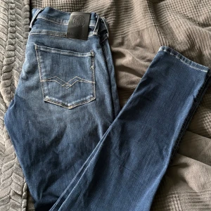 Replay Anbass Hyperflex jeans blå 30/32 - Snygga Replay Anbass Hyperflex jeans i klassisk blå tvätt med lätt slitning, ändast använg någon gång. Modellen har raka ben, fem fickor och dragkedja. Sköna och stretchiga, perfekta för dig som vill ha både stil och komfort. Tidlös design med coola detaljer på bakfickan.