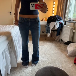 Blå bootcut jeans låg midja - Snygga blå jeans med bootcut och låg midja. Klassisk femficksmodell med dragkedja och knapp framtill. Jeansen har en lätt utsvängd passform nertill och är tillverkade i ett mjukt denimtyg som sitter skönt på kroppen.