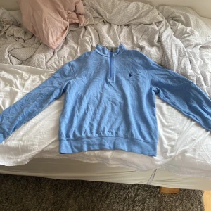 Blå half zip tröja från Polo Ralph Lauren - Säljer en blå långärmad tröja från Polo Ralph Lauren med half zip och klassisk broderad logga på bröstet. Tröjan har en normal passform och är tillverkad i mjuk bomull, perfekt för lager-på-lager under kyliga dagar. Säljer pågrund av att den är för liten 
